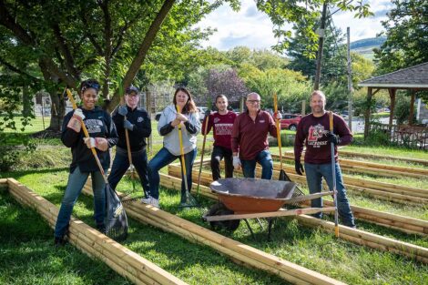 Staff volunteers smile while holding garden rakes and hoes..