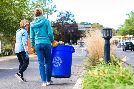 Staff volunteers carry a trash can.