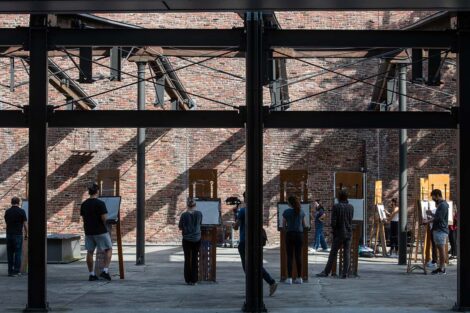 Students stand with easels between dark girders of Ahart Plaza