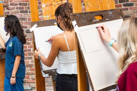 Three students stand in a row with a view of what they are drawing