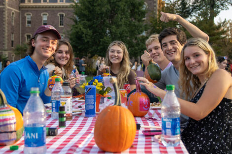 students smile at a table where they are painting pumkins
