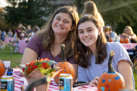students smile at a table where they are painting pumkins