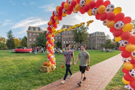 students walk under balloon arch with Pardee behind them