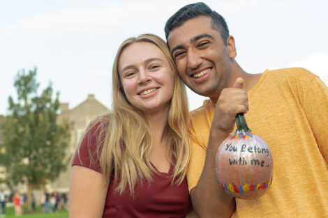 students smile and hold a small pumpkin together