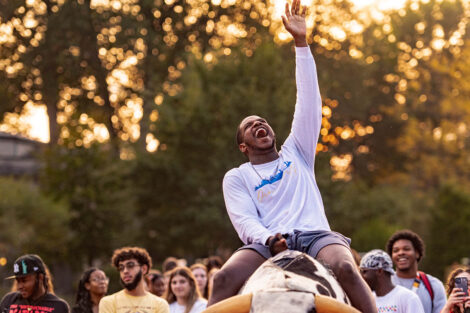 student on a mechanical bull smiles and raises hand in air