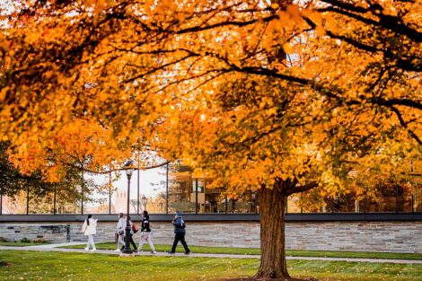 group of people walk past Skillman library, orange foliage