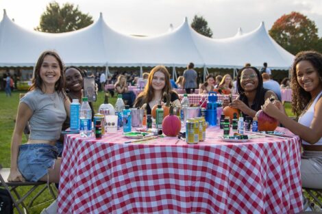 students smile at a table where they are painting pumkins