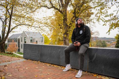student sits on a wall near the Societe d'Honneur plaza, golden foliage in background