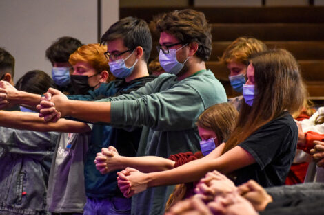 Students hold their hands together and close their eyes during hypnotist Erick Kand's performance.
