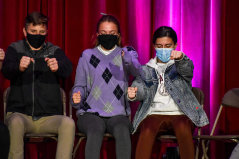 Students, masked and closing their eyes, pretend to drive cars.