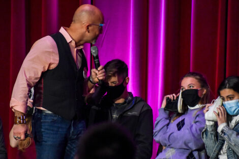 Hypnotist Erick Kand speaks to students, who hold their shoes to their ears.