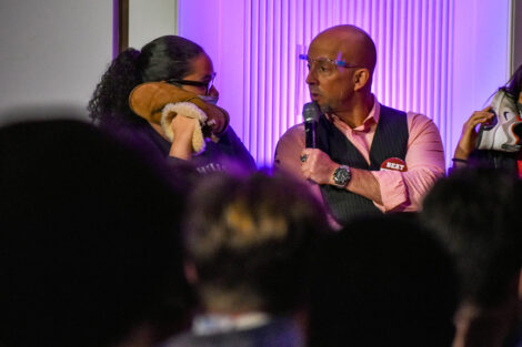 Hypnotist Erick Kand speaks to a student who is holding their shoe to their ear.