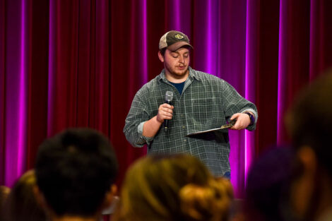A person reads from a clipboard at a microphone.
