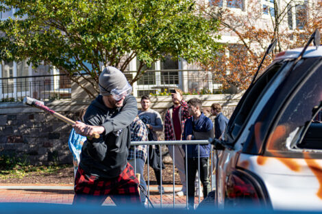 A student hits an SUV with a sledgehammer.