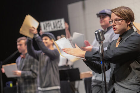 student performers in vintage clothing perform on stage with retro microphones
