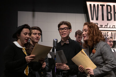 student performers in vintage clothing perform on stage with retro microphones