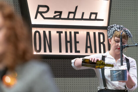 student in vintage dress pours bottle of liquid close to vintage microphone