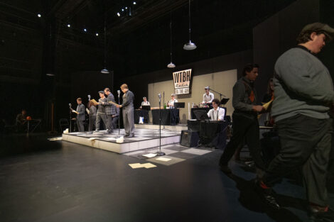 student performers in vintage dress gather on stage with vintage microphones