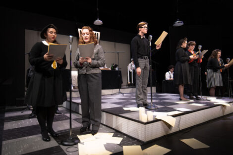 student performers in vintage dress gather on stage with vintage microphones