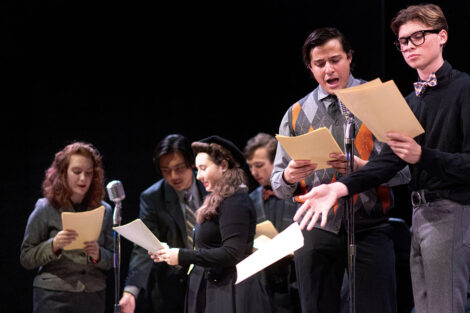 student performers in vintage dress gather on stage with vintage microphones