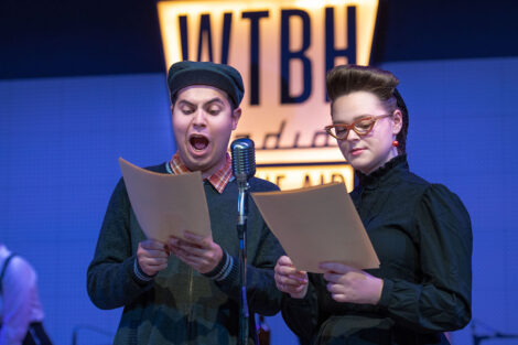student performers in vintage dress gather on stage with vintage microphones