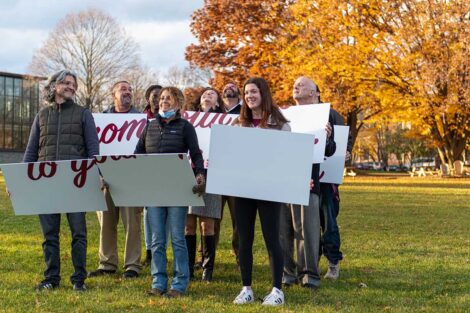 group of people hold signs in formation on Quad and look up and smile