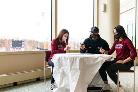 videographer captures two students and coach Ryan Adams painting a sign in Kirby Sports Center