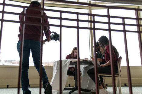 videographer captures two students and coach Ryan Adams painting a sign in Kirby Sports Center