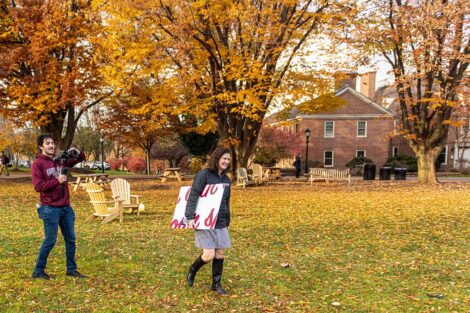 President Hurd walks across the Quad with sign tucked under her arm while videographer trails her