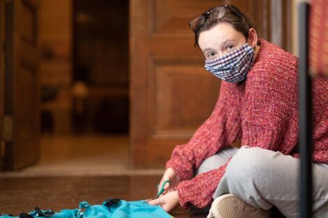 A student in a mask uses scissors to cut lines in fleece to create a blanket