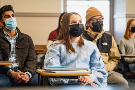 Students, wearing masks, sit inside of a classroom.
