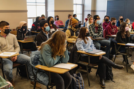Students, wearing masks, take notes in a classroom.