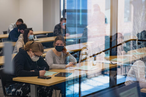 Students, wearing masks, sit inside of a classroom.