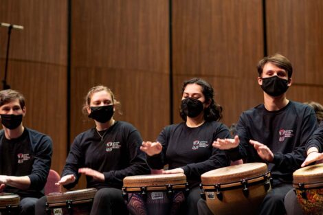 students sit in a line and hit their drums