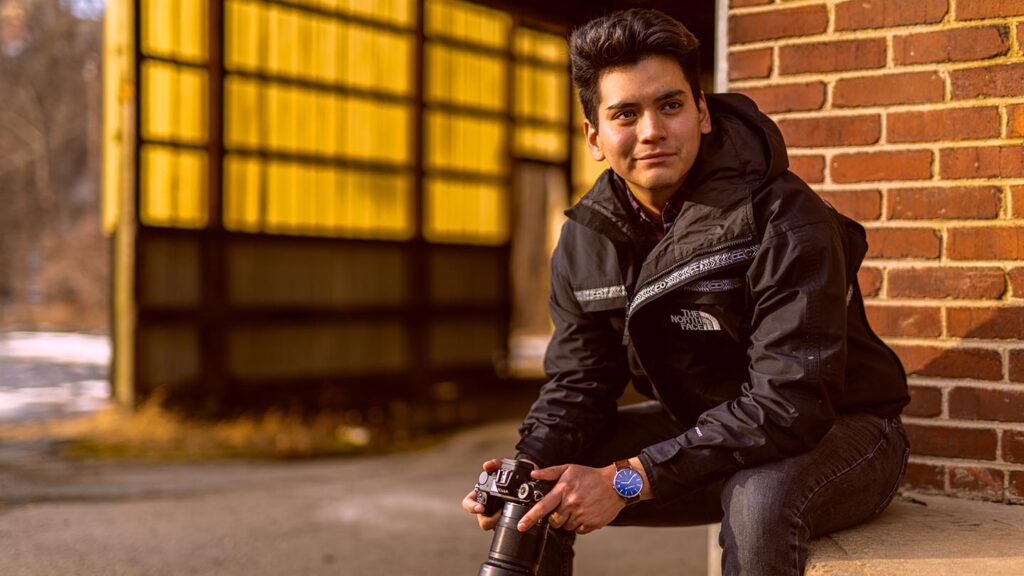Student sits outside holding a camera