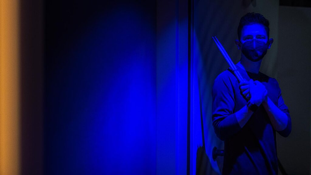 Bathed in blue light, student stands holding drum sticks