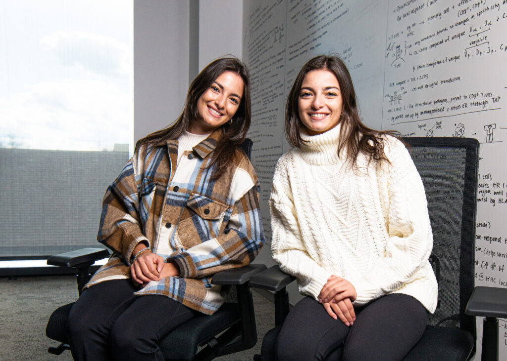 Identical twin Lafayette students Samantha and Stephanie Papalia sitting next to each other in a classroom in front of a white board