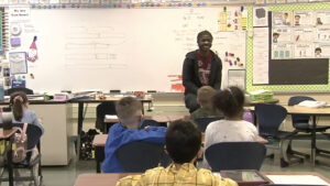 Carl Smith sits on a desk in an elementary school classroom