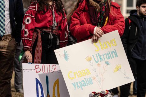 students gather with signs supporting Ukraine, two students dressed in traditional Ukrainian clothing and head accessories