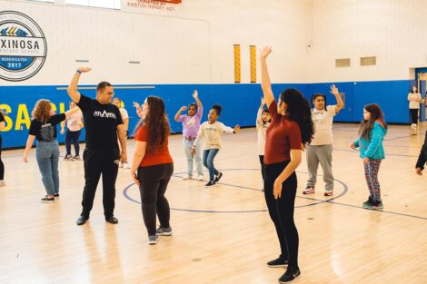 group of Lafayette students and elementary school students raise their hands and dance in gymnasium