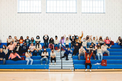 elementary school students and Lafayette students sit together in the stands in gymnasium