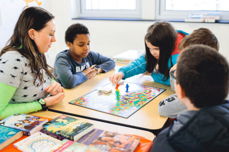 Lafayette student sits with elementary students playing a board game