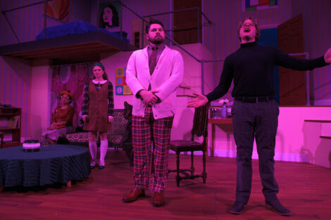 students in a stage production act on stage with pink dramatic lighting
