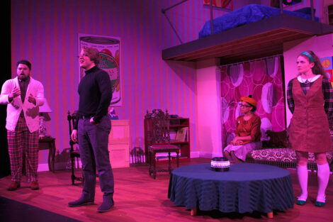 students in a stage production act on stage with pink dramatic lighting