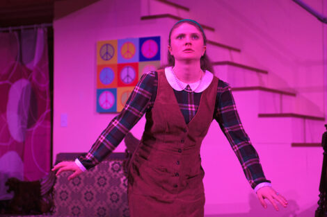 students in a stage production act on stage with pink dramatic lighting
