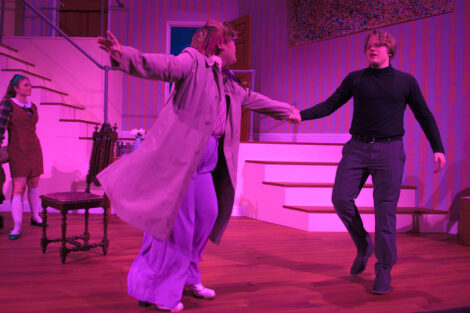 students in a stage production act on stage with pink dramatic lighting