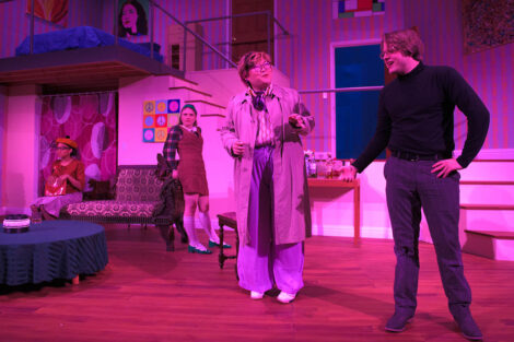 students in a stage production act on stage with pink dramatic lighting