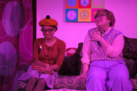 students in a stage production act on stage with pink dramatic lighting