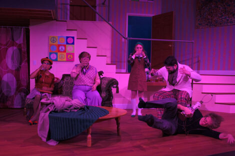 students in a stage production act on stage with pink dramatic lighting
