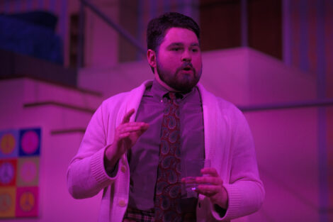 students in a stage production act on stage with pink dramatic lighting